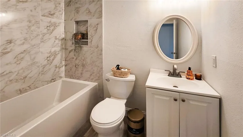 Bathroom with a textured wall, vanity, and shower / washtub combination