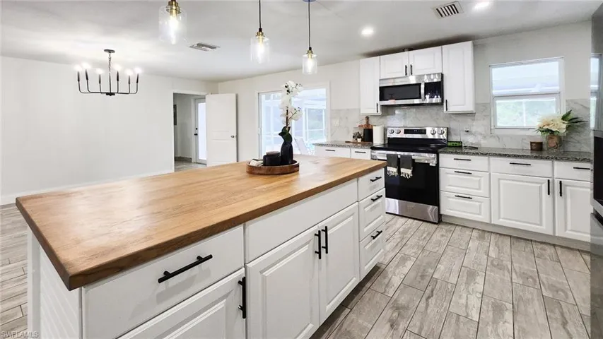 Kitchen with stainless steel appliances, white cabinets, wood finish floors, wood counters, and backsplash