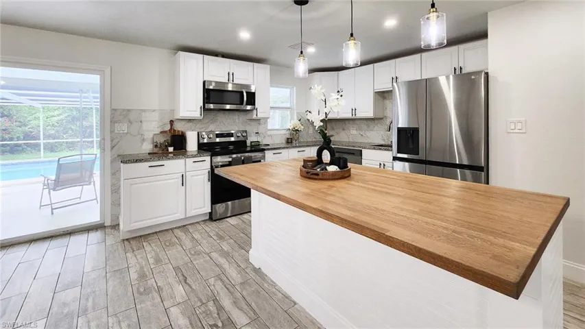 Kitchen with stainless steel appliances, decorative light fixtures, white cabinetry, wood tiled floors, and a kitchen island
