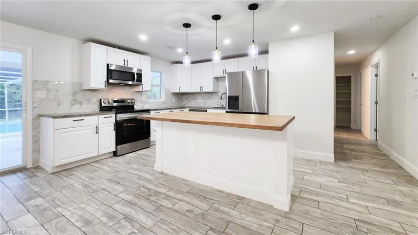 Kitchen featuring stainless steel appliances, white cabinetry, decorative light fixtures, and wood tiled floors