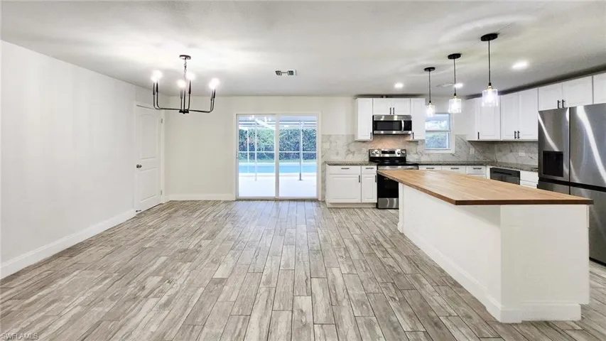 Kitchen with butcher block countertops, stainless steel appliances, wood tiled floors, white cabinets, and suspended lighting