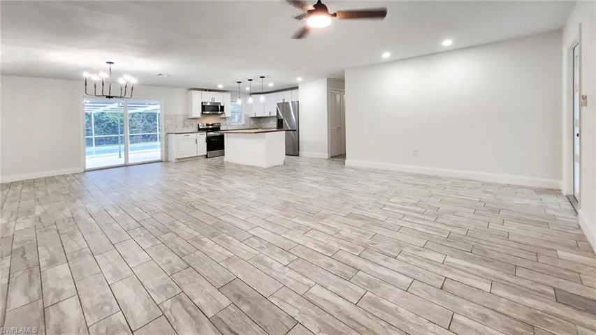 Unfurnished living room with a ceiling fan, wood finish floors, and hanging lights