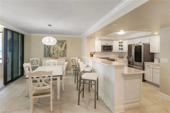 Kitchen featuring stainless steel appliances, ornamental molding, glass insert cabinets, white cabinetry, and a peninsula
