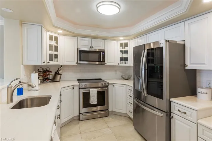 Kitchen with stainless steel appliances, a sink, tasteful backsplash, a raised ceiling, and white cabinetry