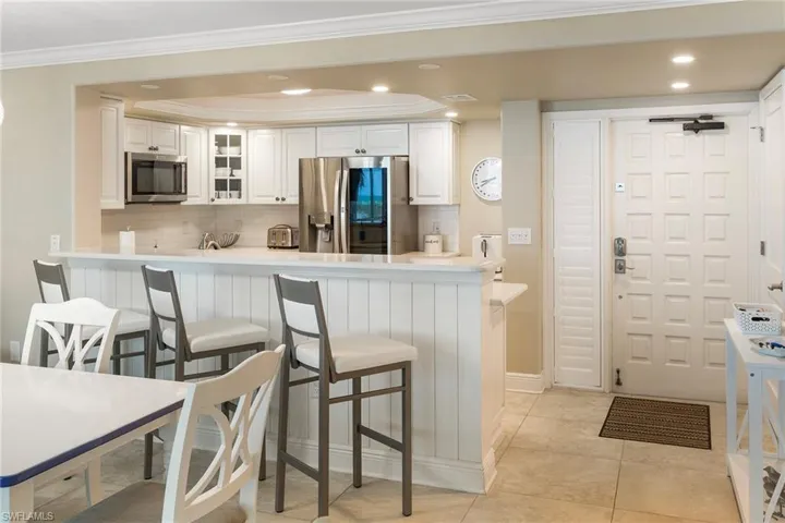 Kitchen featuring appliances with stainless steel finishes, a kitchen bar, tasteful backsplash, white cabinetry, and crown molding