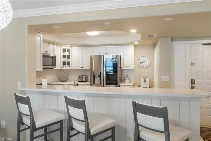 Kitchen with appliances with stainless steel finishes, tasteful backsplash, glass insert cabinets, light countertops, and a kitchen breakfast bar