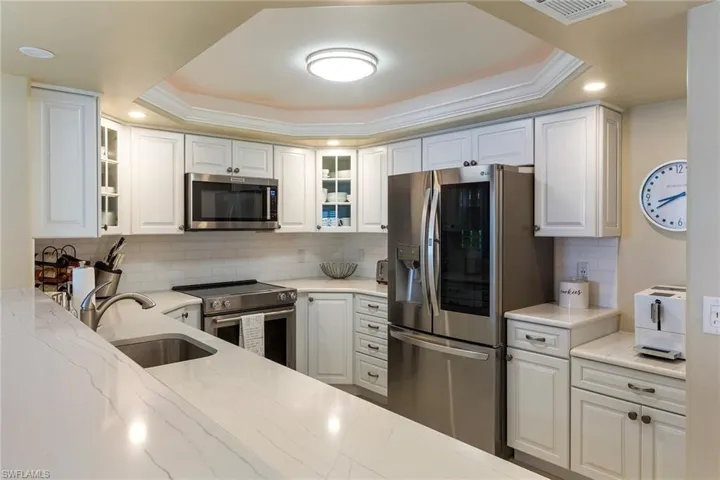Kitchen featuring stainless steel appliances, a tray ceiling, light stone counters, decorative backsplash, and white cabinets