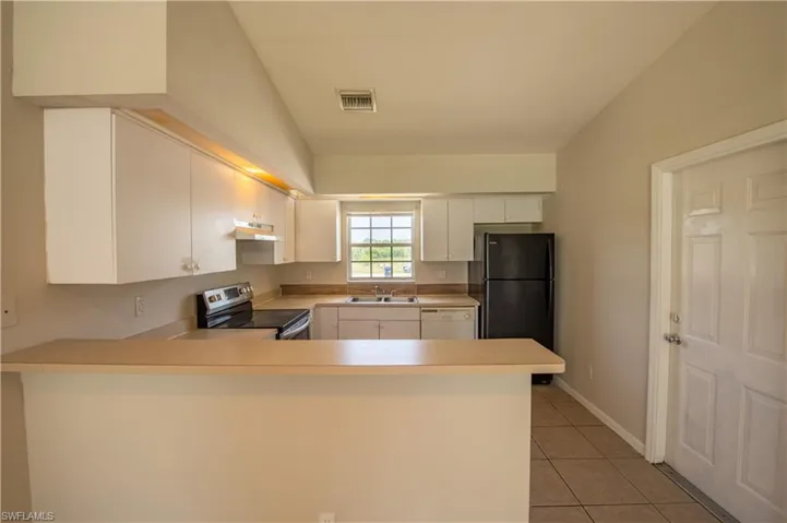 Kitchen featuring white cabinetry, light-toned countertops, tile flooring, and a window above the sink