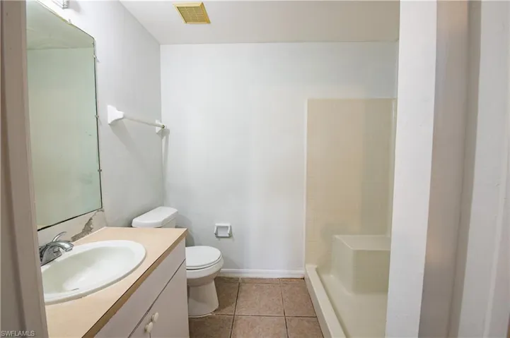 Bathroom featuring a shower stall with built-in seating, a single vanity with an integrated sink, a large wall-mounted mirror, and tile flooring