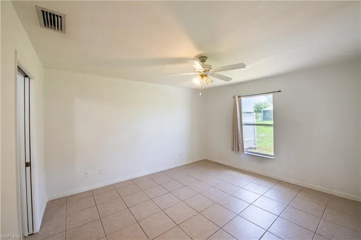 Room featuring ceramic tile flooring, a window providing natural illumination, a ceiling fan with integrated lighting, and a neutral color palette