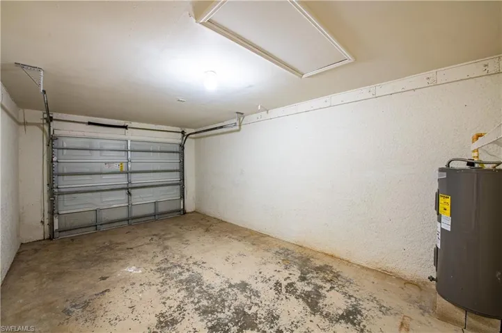 Attached single-car garage featuring a roll-up door, exposed ceiling joists, and a water heater