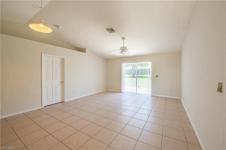 Spacious room featuring vaulted ceilings, light tile flooring, white vertical blinds, and a ceiling fan
