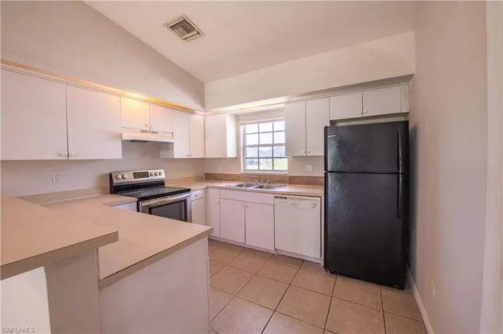 Kitchen featuring white cabinetry, a built-in electric range, a black refrigerator, a white dishwasher, and light-toned tile flooring