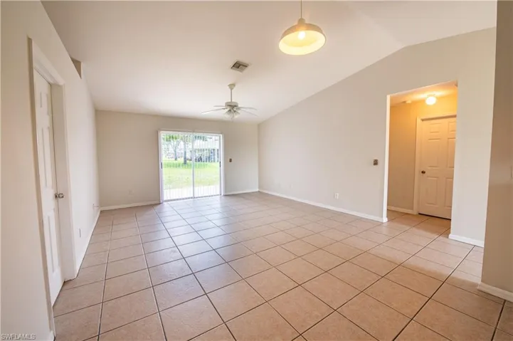 Spacious living area featuring neutral-toned tile flooring, vaulted ceilings, and a ceiling fan