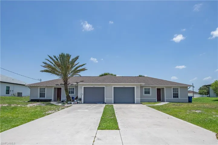 Duplex property featuring a light gray exterior, individual garage doors, separate entry doors, and a concrete driveway