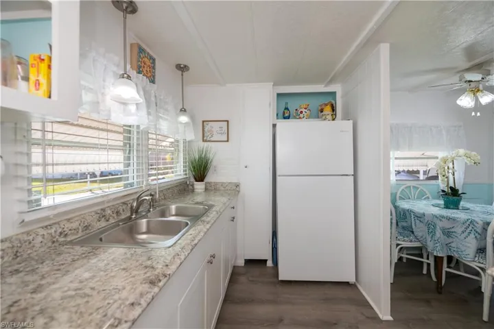 Kitchen with dark wood-type flooring, sink, hanging light fixtures, white fridge, and white cabinetry
