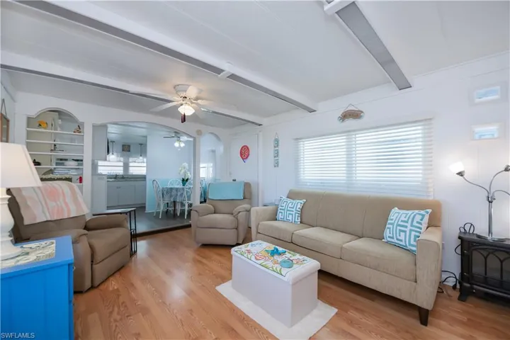 Living room featuring beamed ceiling, built in shelves, ceiling fan, and light wood-type flooring