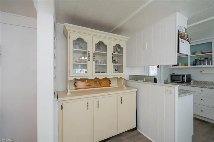 Dining with white cabinets, dark hardwood / wood-style flooring, and light stone countertops