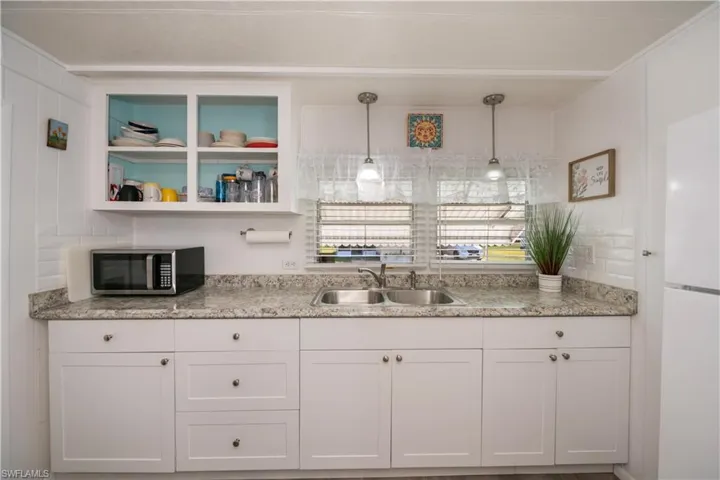 Kitchen with light stone countertops, sink, pendant lighting, white fridge, and white cabinetry