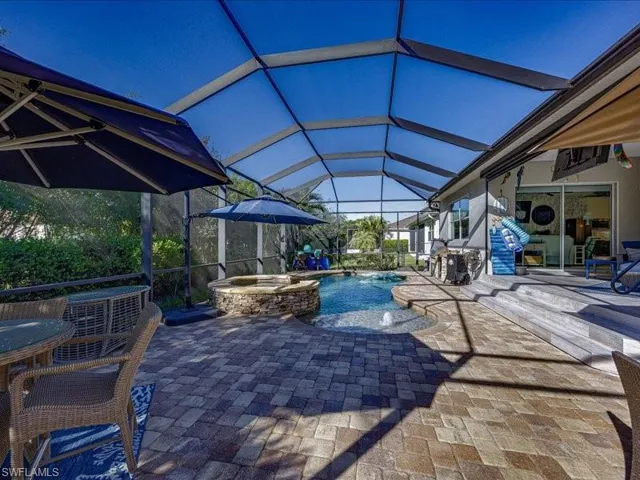 Screened outdoor living area featuring a paver patio, integrated spa, and swimming pool with water features
