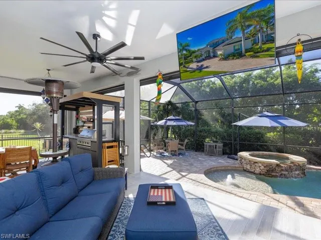Screened lanai featuring wood-finish flooring, a built-in outdoor kitchen, a large ceiling fan, and a stone-accented spa with water feature