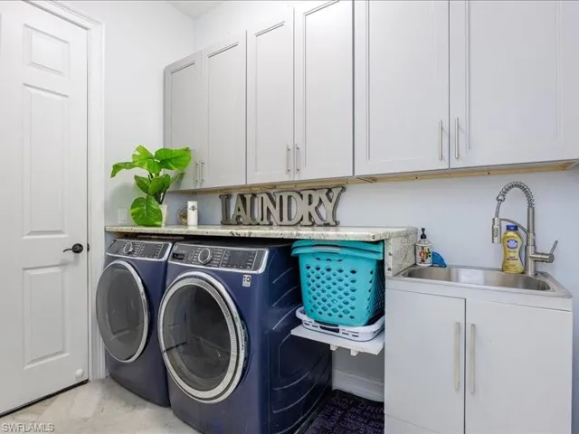 Dedicated laundry area featuring upper and lower cabinetry, stone-finish countertops, stainless steel utility sink, and wall-mounted faucet