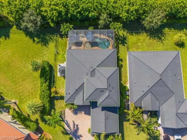 Expansive property featuring a screened-in pool, lush green lawn, mature landscaping, and a multi-gabled roofline