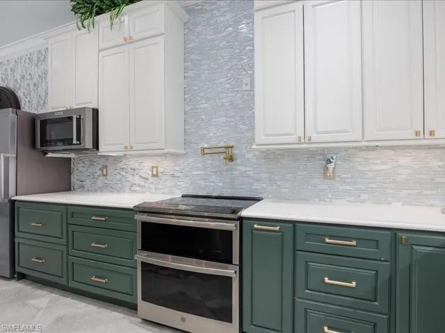 Kitchen featuring two-tone cabinetry with white upper cabinets and green lower cabinets, stainless steel appliances, white countertops, and a full-height tile backsplash with a linear pattern