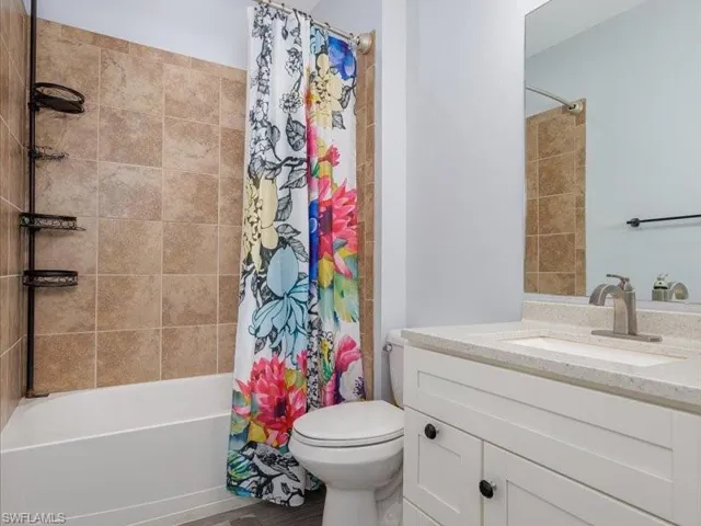 Bathroom featuring a white tub, natural-toned tile surround, and a white vanity with a light speckled countertop