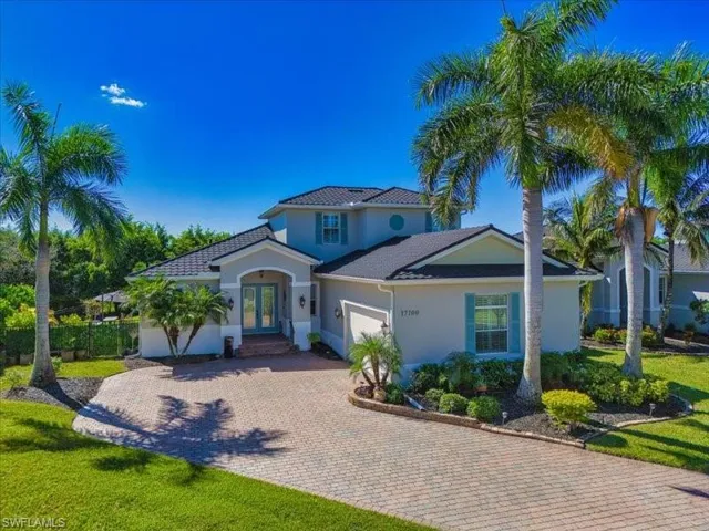 Stucco exterior with a tiled roof, featuring a paver driveway, mature palm trees, and established landscaping
