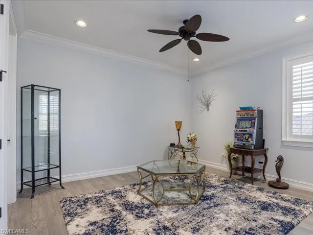 Bright interior space featuring wood-finish flooring, a ceiling fan, recessed lighting, crown molding, and plantation shutters