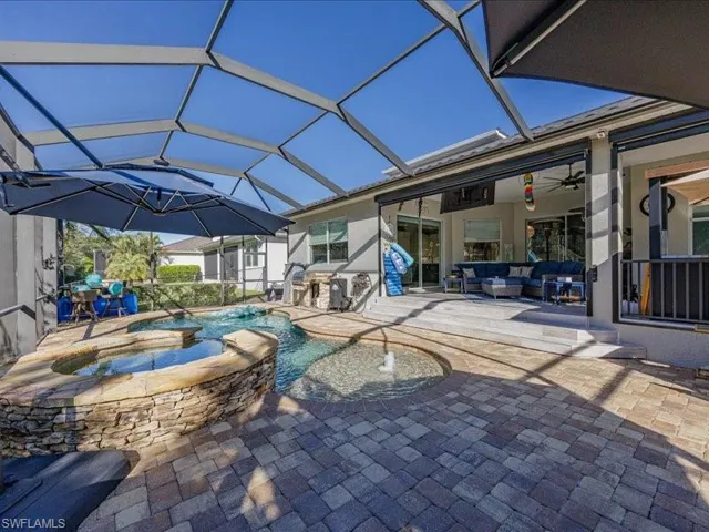 Screened lanai featuring a paver patio, a stone-clad spa and pool with water features, an outdoor kitchen with built-in cabinetry, and a covered porch with sliding glass doors