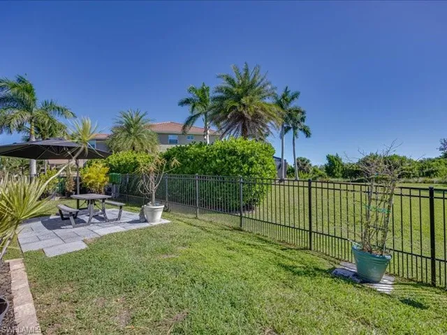 Expansive grassy yard featuring a black metal perimeter fence and a stone paver patio