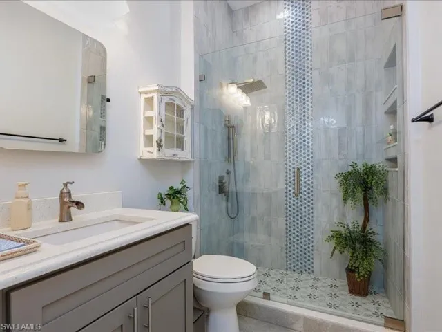 Modern bathroom featuring a glass-enclosed shower with contrasting tile inlay, built-in shower niches, a rainfall showerhead, and a vanity with an integrated sink and quartz countertop