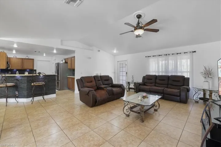 Living room with light tile patterned flooring, visible vents, ceiling fan, and vaulted ceiling