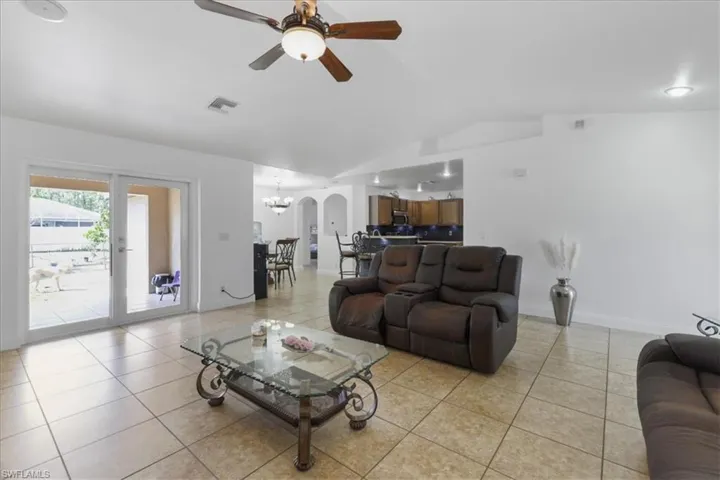 Living room featuring light tile patterned floors, visible vents, lofted ceiling, and ceiling fan with notable chandelier