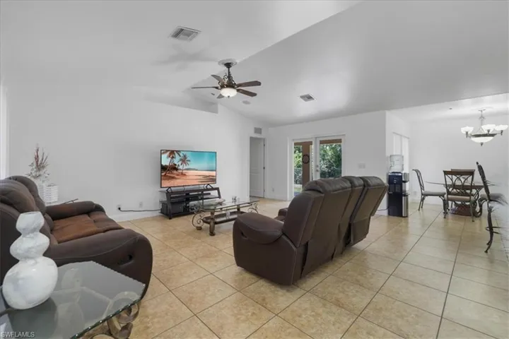 Living area featuring light tile patterned floors, visible vents, vaulted ceiling, and ceiling fan with notable chandelier