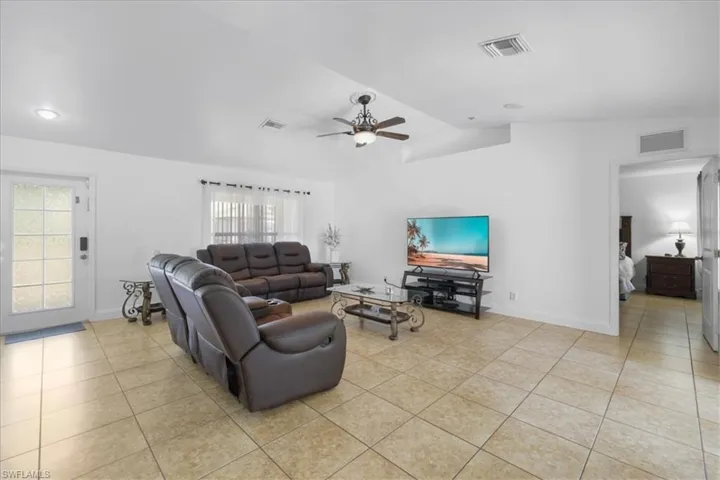 Living room with light tile patterned floors, visible vents, a ceiling fan, and vaulted ceiling