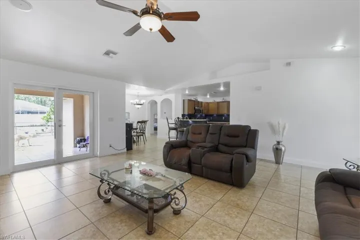 Living area with arched walkways, light tile patterned floors, ceiling fan with notable chandelier, visible vents, and lofted ceiling