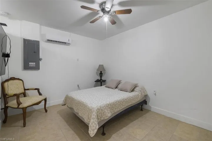 Bedroom with light tile patterned floors, electric panel, a wall mounted AC, baseboards, and a ceiling fan