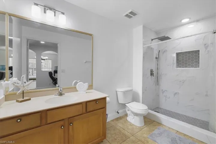 Full bath with ensuite bath, toilet, vanity, visible vents, and a marble finish shower