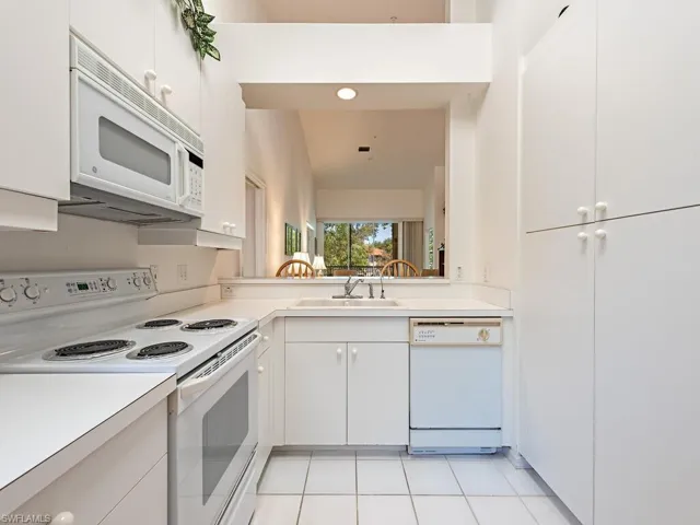 Kitchen with a sink, light countertops, light tile patterned floors, white appliances, and white cabinetry