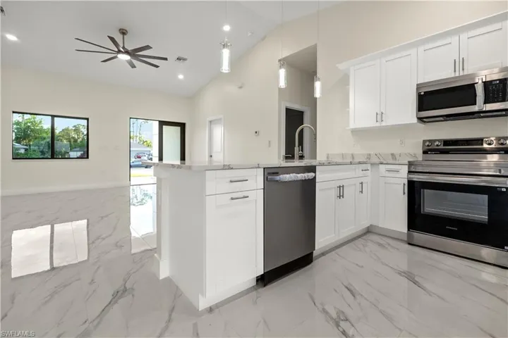 Kitchen featuring stainless steel appliances, open floor plan, white cabinets, light marble finish flooring, and high vaulted ceiling