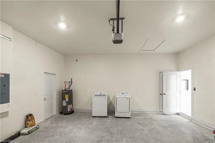 Garage with electric panel, water heater, separate washer and dryer, and a garage door opener