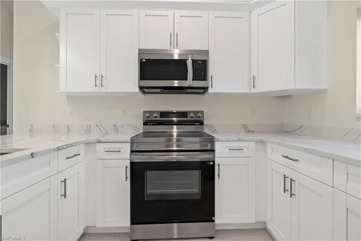 Kitchen with appliances with stainless steel finishes, light stone countertops, white cabinetry, and light marble finish flooring