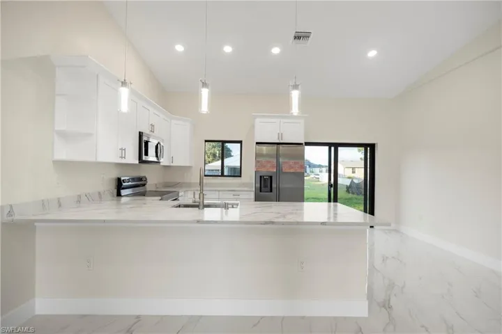 Kitchen featuring a peninsula, appliances with stainless steel finishes, light stone countertops, white cabinetry, and recessed lighting