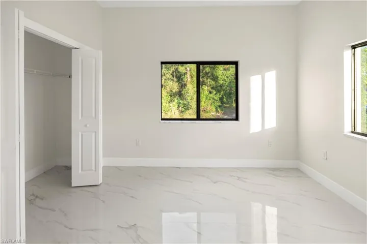 Unfurnished bedroom with light marble finish floors and a walk in closet