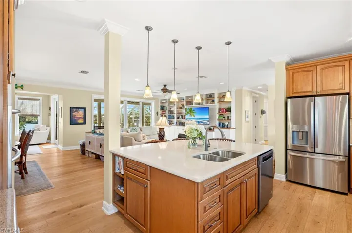 Kitchen featuring crown molding, appliances with stainless steel finishes, light wood-style flooring, brown cabinetry, and open floor plan