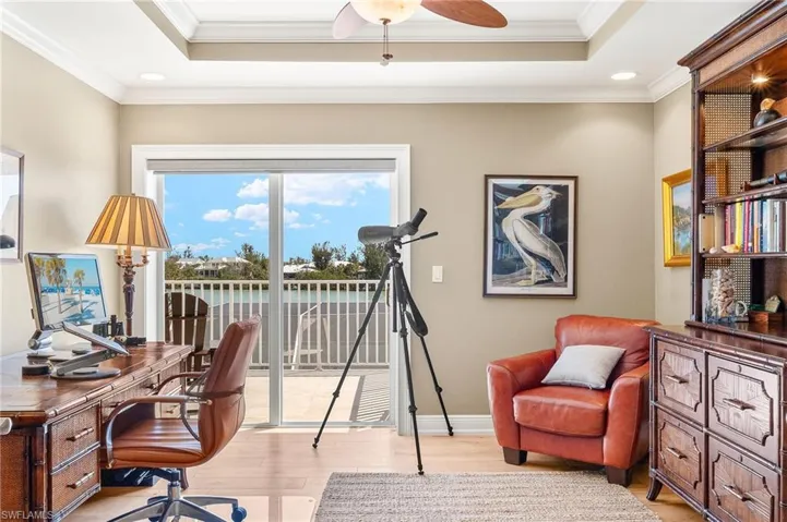 Office area featuring light wood-type flooring, a tray ceiling, crown molding, recessed lighting, and a ceiling fan