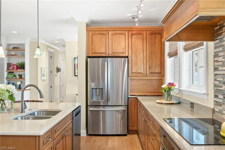 Kitchen featuring stainless steel appliances, brown cabinets, light wood-type flooring, decorative light fixtures, and crown molding